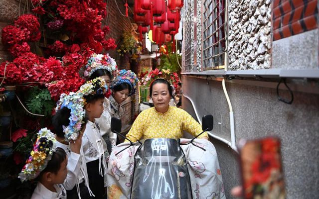 图3  2025年8月18日，在蟳埔村，一名蟳埔女骑电动车从几名体验“簪花围”妆造的游客前经过。新华社记者 肖潇 摄.jpg